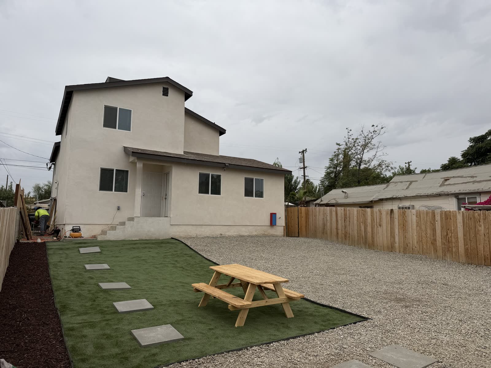 The back of the two-story house, with a patch of lawn, a picnic table and a fenced gravel yard